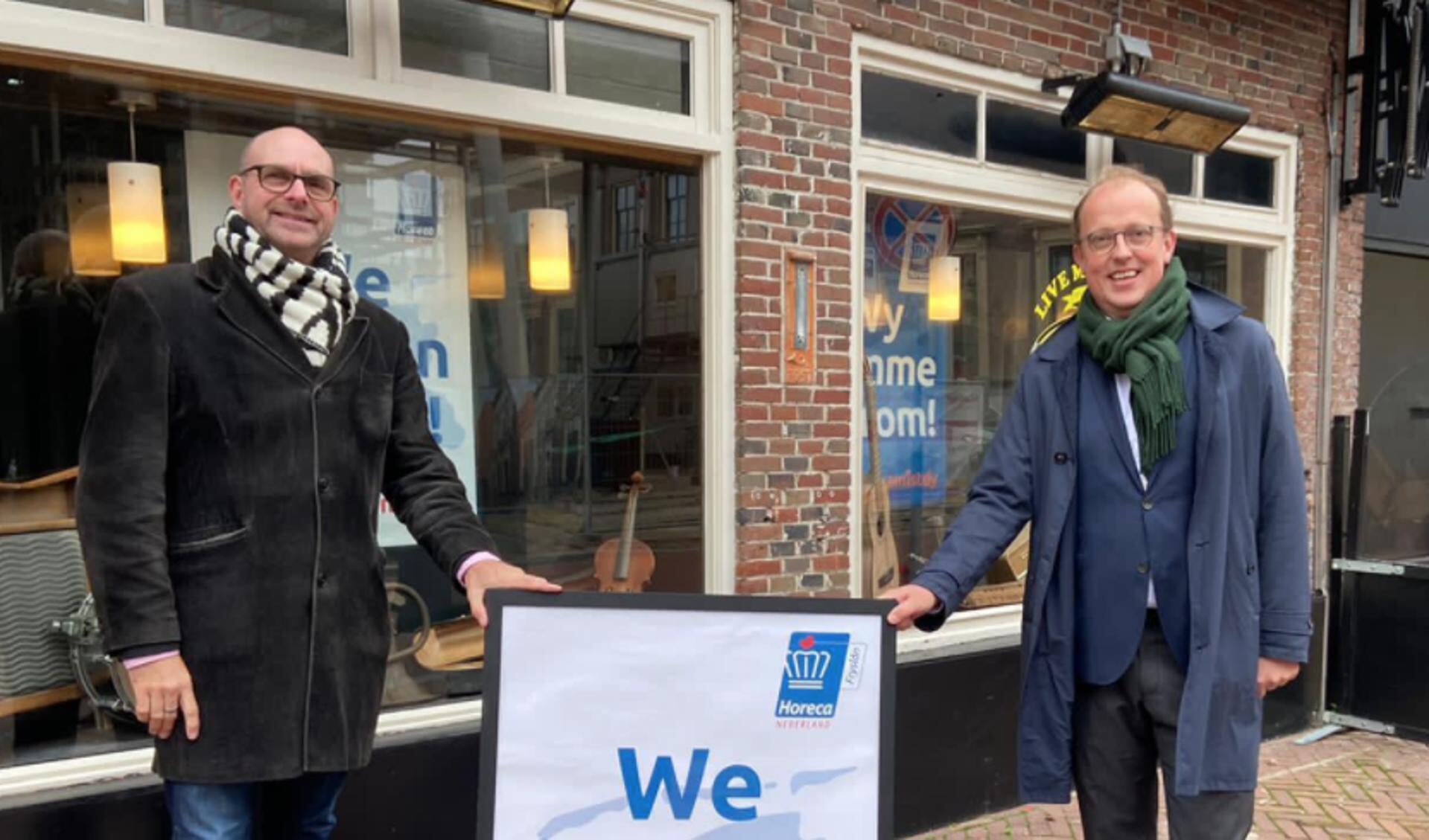 KHN Friesland-voorzitter Ton Eijer (links) overhandigt Leeuwarder wethouder Fruiso Douwstra een symbool van de actie.