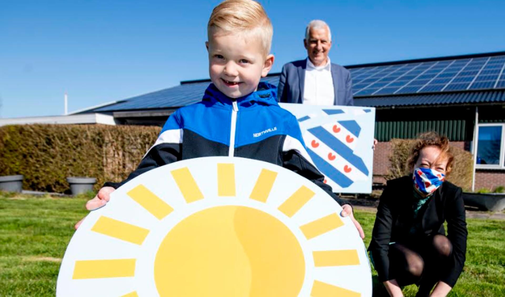 Gedeputeerde Sietske Poepjes en wethouder Bert Wassink overhandigen Jelte met de symbolische zon een duurzame toekomst in Fryslân toe.