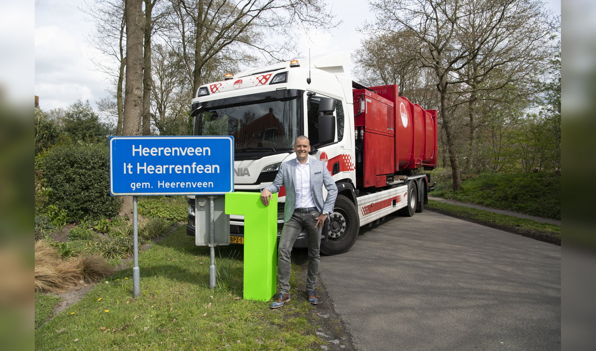 Wethouder Jaap van Veen poseert samen met een Omrin-vuilniswagen bij een bord van Heerenveen.