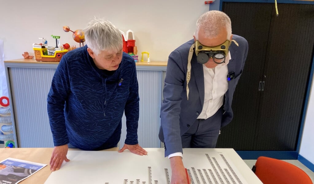 Wethouder Bert Wassink oefent stemmen met een stem- mal, met behulp van Hilda Snippe (voorzitter Werkgroep Toegankelijkheid gemeente Leeuwarden). Hiervoor draagt hij een simulatiebril. Deze bril bootst een visuele beperking na, waarbij het lijkt alsof je door een kokertje kijkt. 