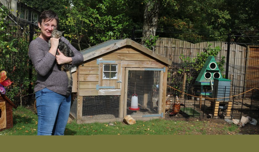 Arianne met Zus haar armen in de tuin van Het Katshuisch, waar de katten alle ruimte hebben. Al moeten ze die ruimte wel delen met de kippen.
