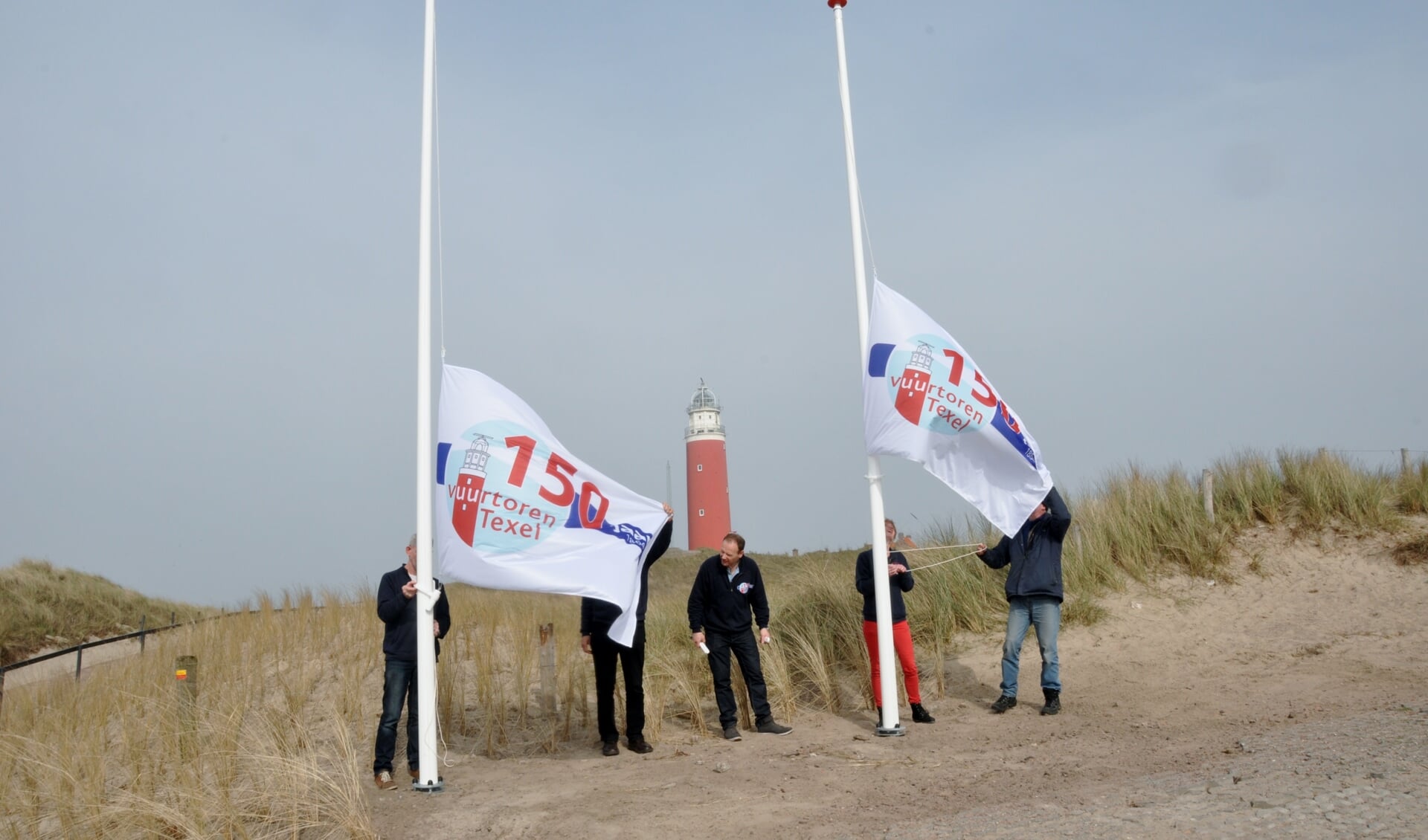 Medewerkers van Stichting Texels Museum hijsen de jubileumvlaggen bij de nieuwe entree van de vuurtoren.