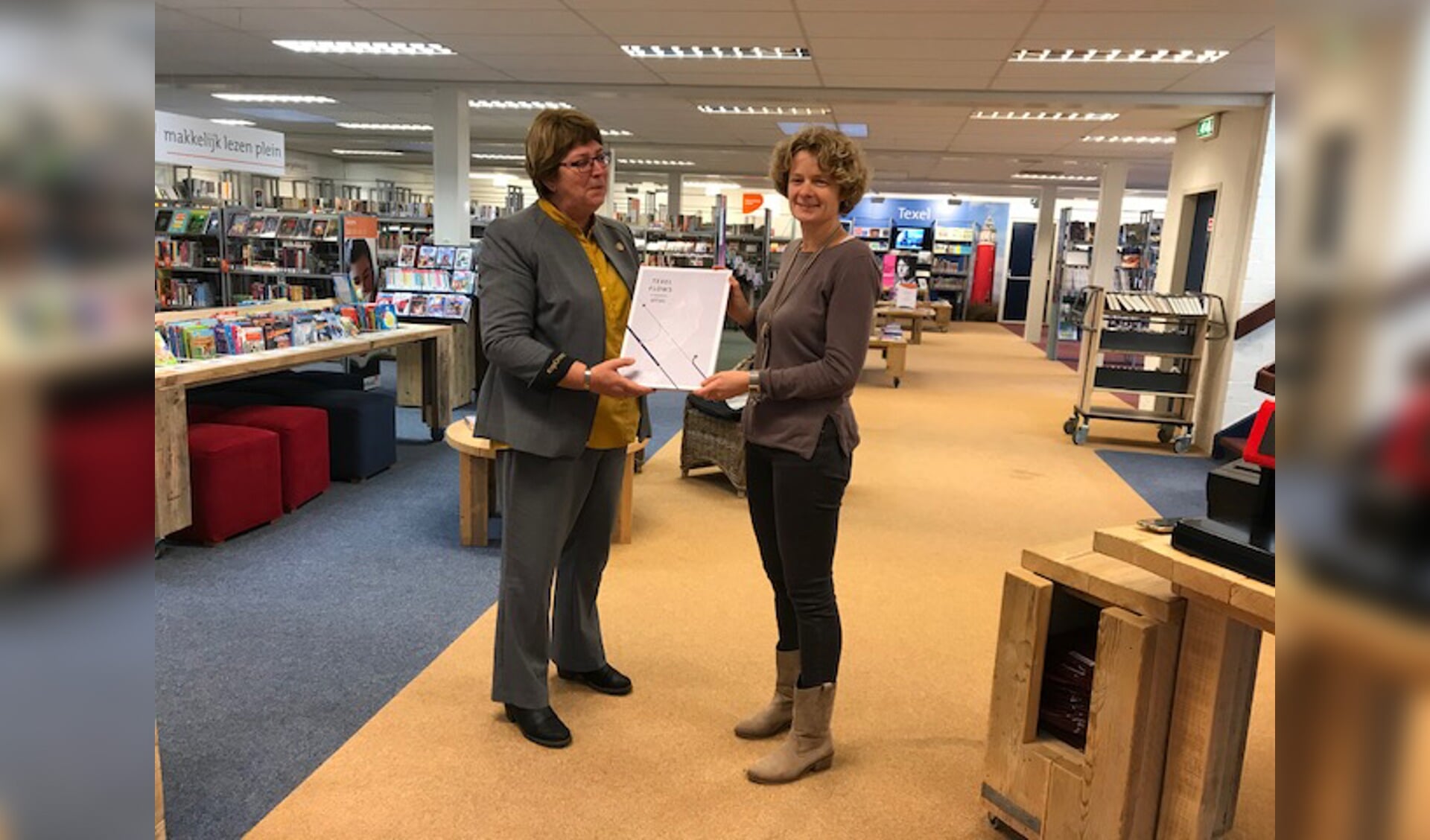 Marion Barth (rechts) van het Texelfonds overhandigt de atlas aan Maaike Vonk van de bibliotheek. 