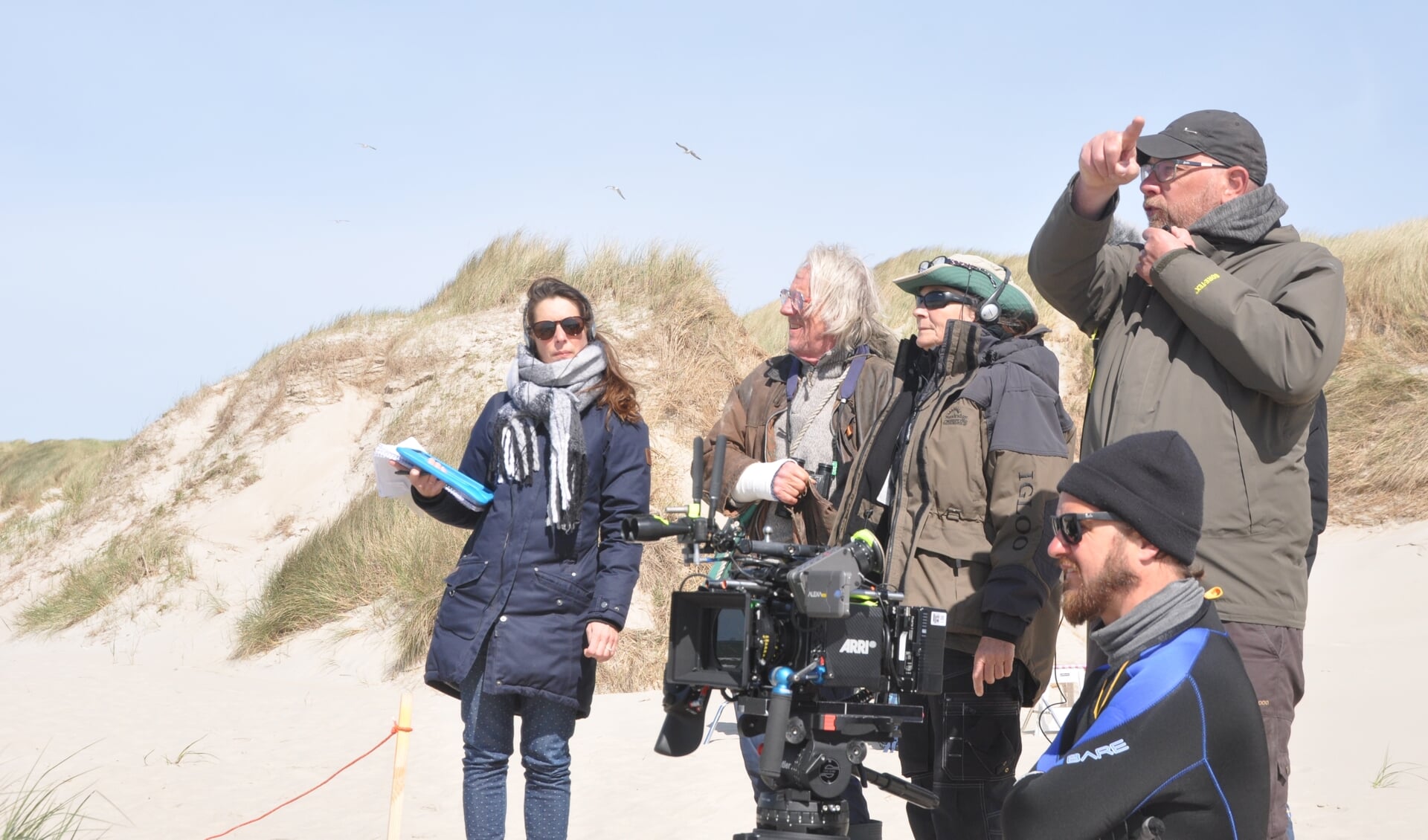 Freek de Jonge en Threes Anna (met hoed) tijdens het filmen op Texel. Opnameleider René Jonkers (rechts) geeft aanwijzingen aan de crew op het strand.