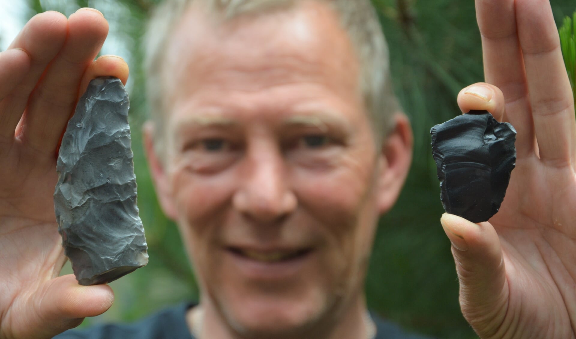 Paul Dekker toont de vuurstenen sikkel (links, 3.500 jaar oud)  en rechts een bladspits (tussen de 40.000 en 125.000 jaar oud). 