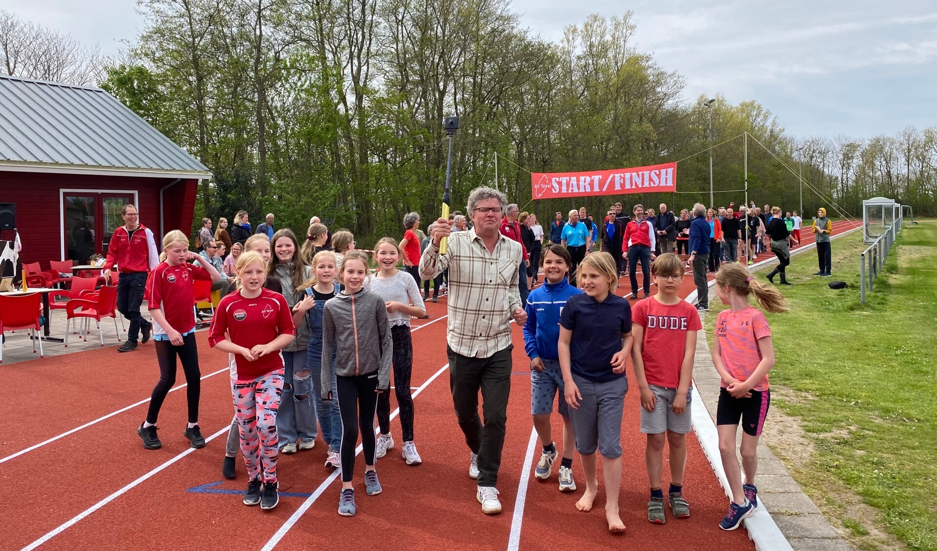 Wethouder Remko van de Belt legt met jonge leden van Atletiekvereniging Texel de laatste meters van de estafette af.