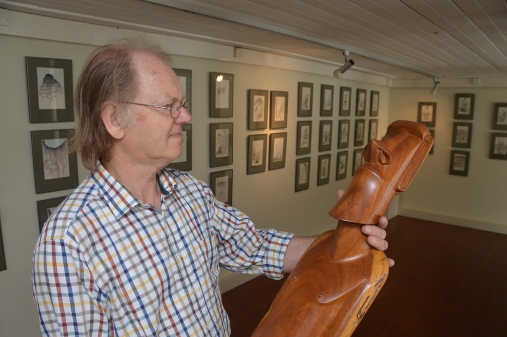 Niek Welboren met een houten beeld van Paaseiland. Op de achtergrond de tekeningen die herinneren aan zijn reis in 1992. 