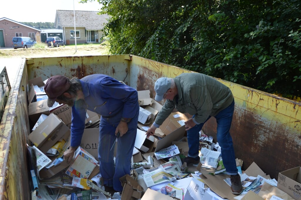 Cor Zijm en Hans Bonewit pletten karton en papier in de Hoornder container. 