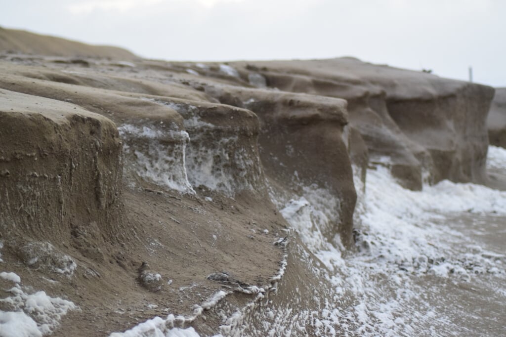 Een bekend beeld van het Texelse strand na een storm: de golven hebben flinke happen uit de duinen genomen. 