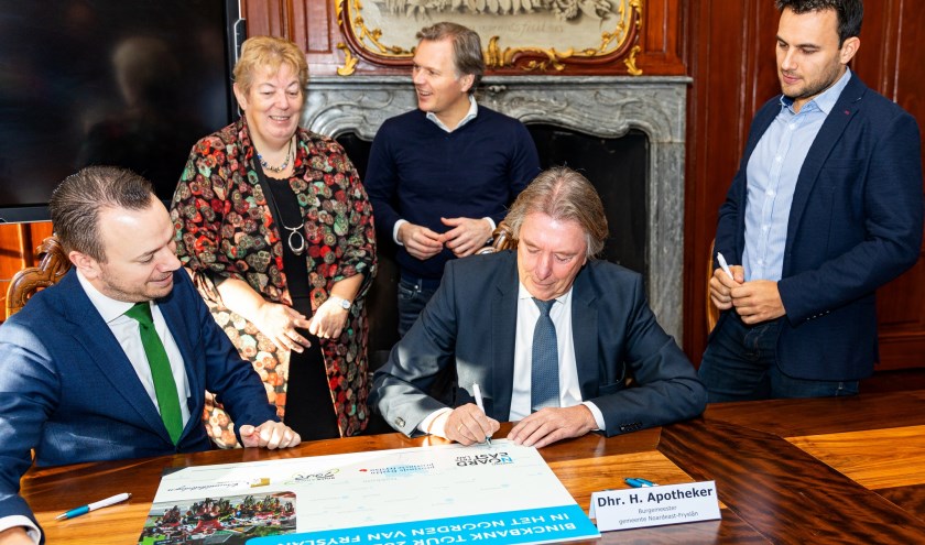 Burgemeester Apotheker tekent de overeenkomst in het bijzijn van organisatoren en collega-bestuurders.