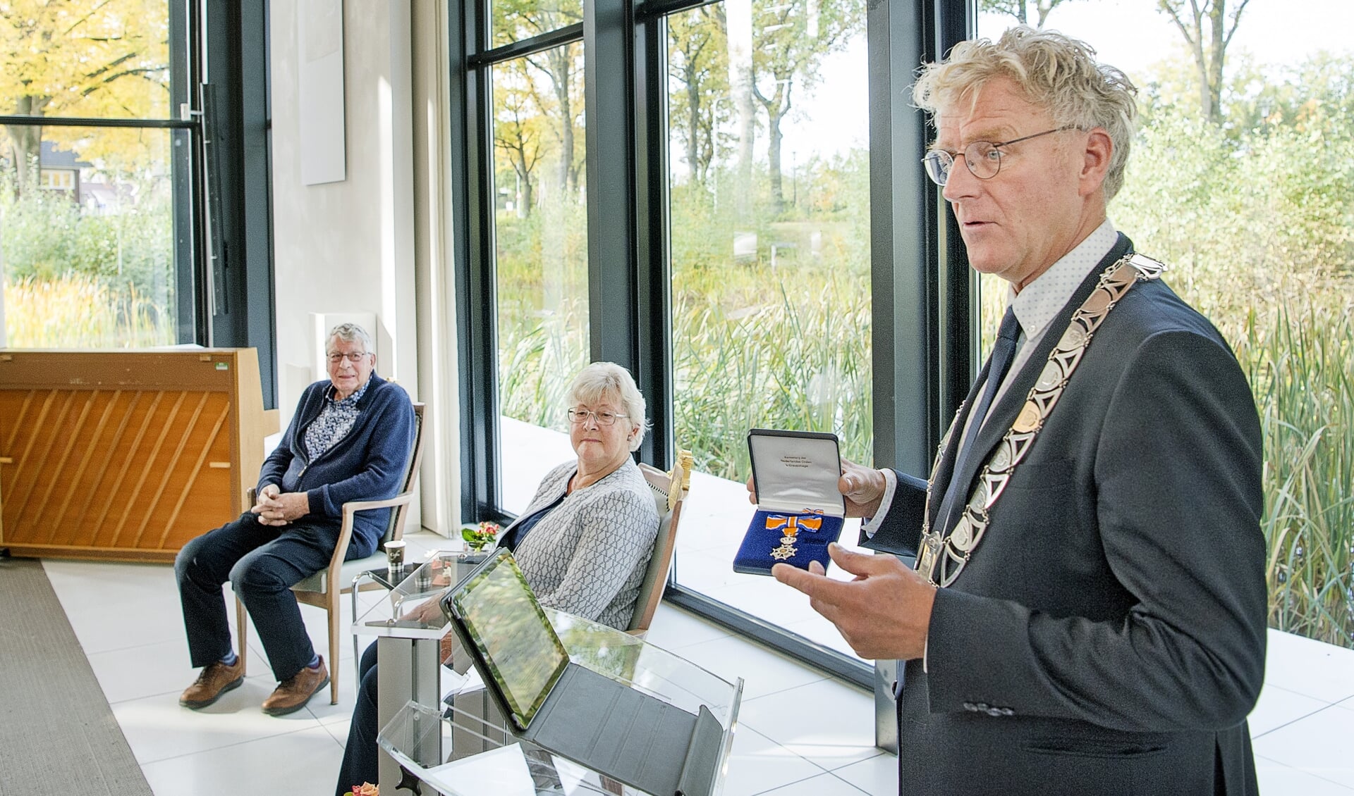 Burgemeester Oebele Brouwer toont de onderscheiding die hij even later overhandigt aan het echtpaar Joop en Menke Land uit Surhuisterveen. 