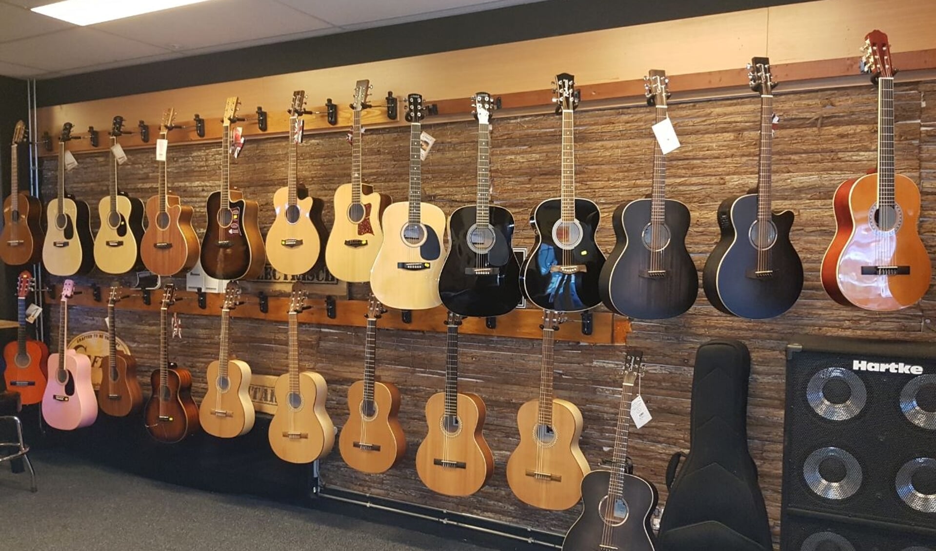 De gitaren in de winkel hangen speelklaar. Heel veel instrumenten zijn daarnaast te bestellen.
