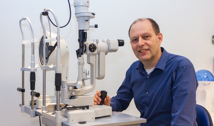 Theo Dijk bij een apparaat waarmee hij contactlenzen meet, maar ook staar kan vaststellen.
