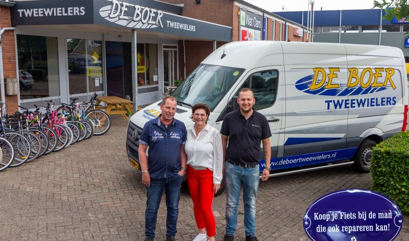 Iede de Boer, Marga de Boer en Daniël de Jong voor de winkel en de bus. Rechtsonder een bordje dat in de winkel aan de toonbank hangt.