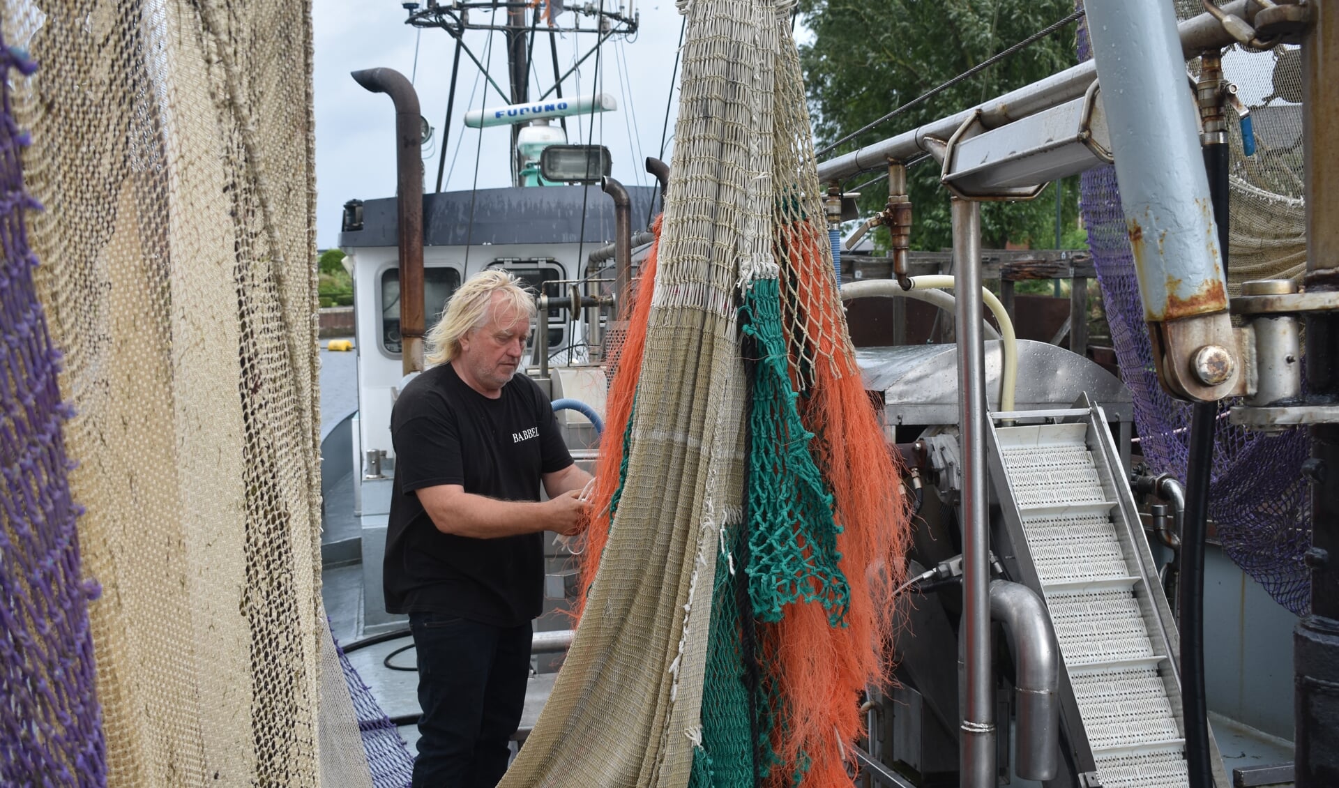 Garnalenvisser Jan de Vries repareert een net op zijn kotter.