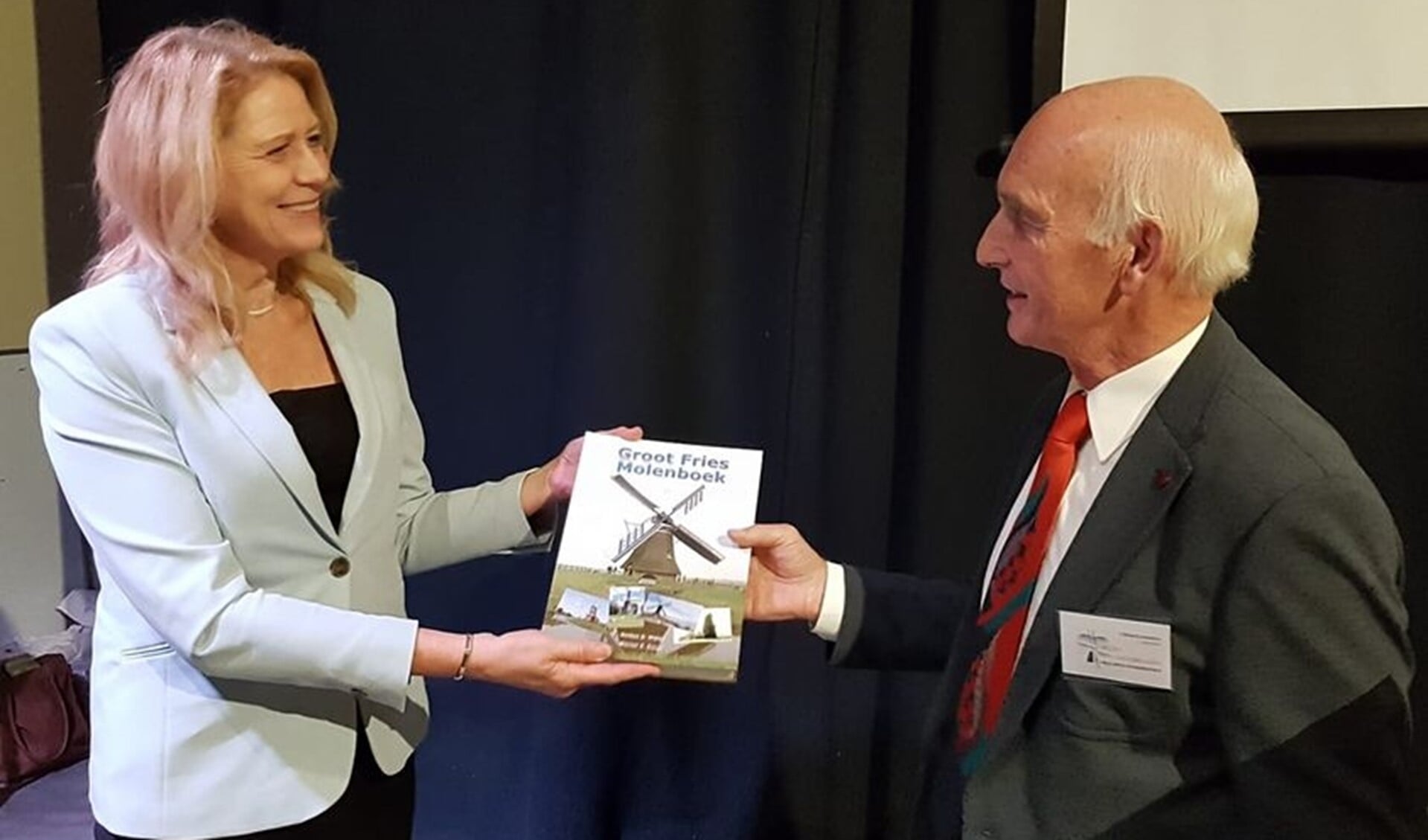 Wiepke Schukken, voorzitter van De Fryske Mole, reikt het eerste exemplaar van het Groot Fries Molenboek uit aan mevrouw Luzette Kroon, de dijkgraaf van Wetterskip Fryslân.