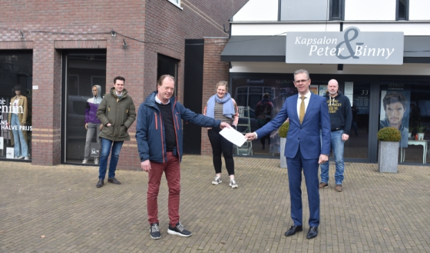 <p>Burgemeester Jeroen Gebben ontvangt van HIMBO-voorzitter Erik Meijer de oproep.<br>Andere HIMBO-bestuurders staan achter hen. Daarachter links Shoeby, dat niet<br>normaal open mag, rechts kapsalon Beter & Binny, die vanaf 3 maart wel open mag.</p>