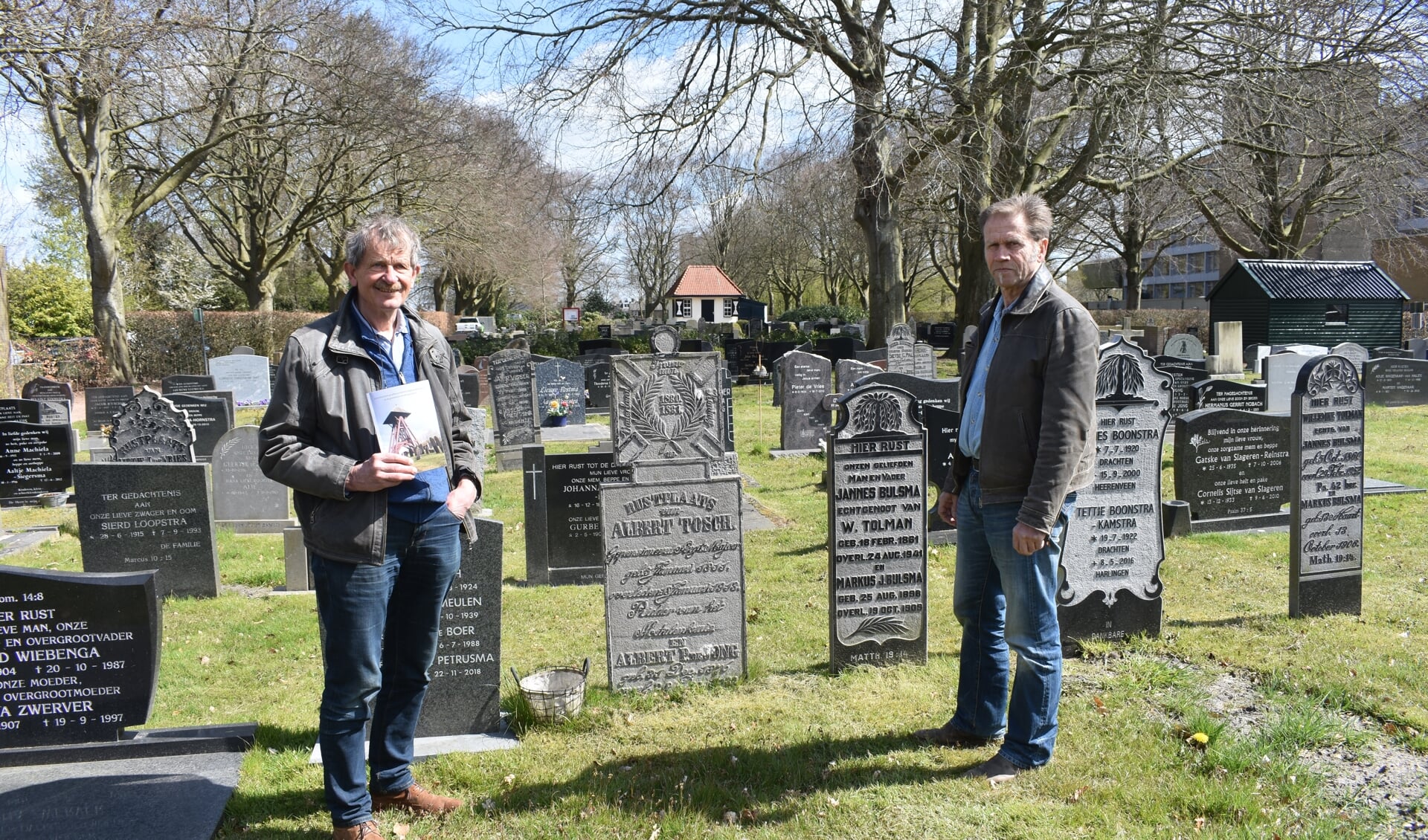 Roelof Hazelhoff (links, met het boekje) en Bé Lamberts op de Zuiderbegraafplaats in Drachten. Tussen hen in de grafsteen voor Albert Tosch.