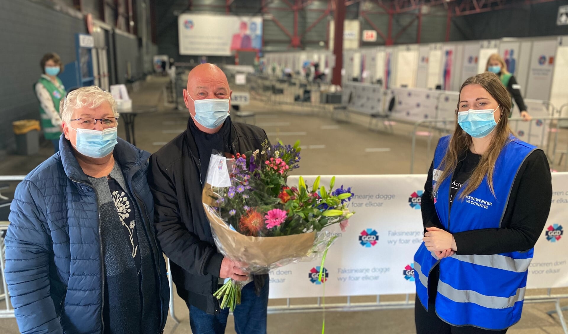 GGD-medewerker Jantina Siegersma overhandigt de heer Dries van der Horst (73) uit Stiens een boeket bloemen. Met zijn vrouw kwam hij voor zijn eerste vaccinatieafspraak naar de Friese hoofdstad.