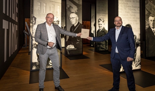 <p>Bestuurder Martin Kirchner van Noorderbreedte (links) overhandigt het boek aan Kris Callens, in het Fries Verzetsmuseum.</p>