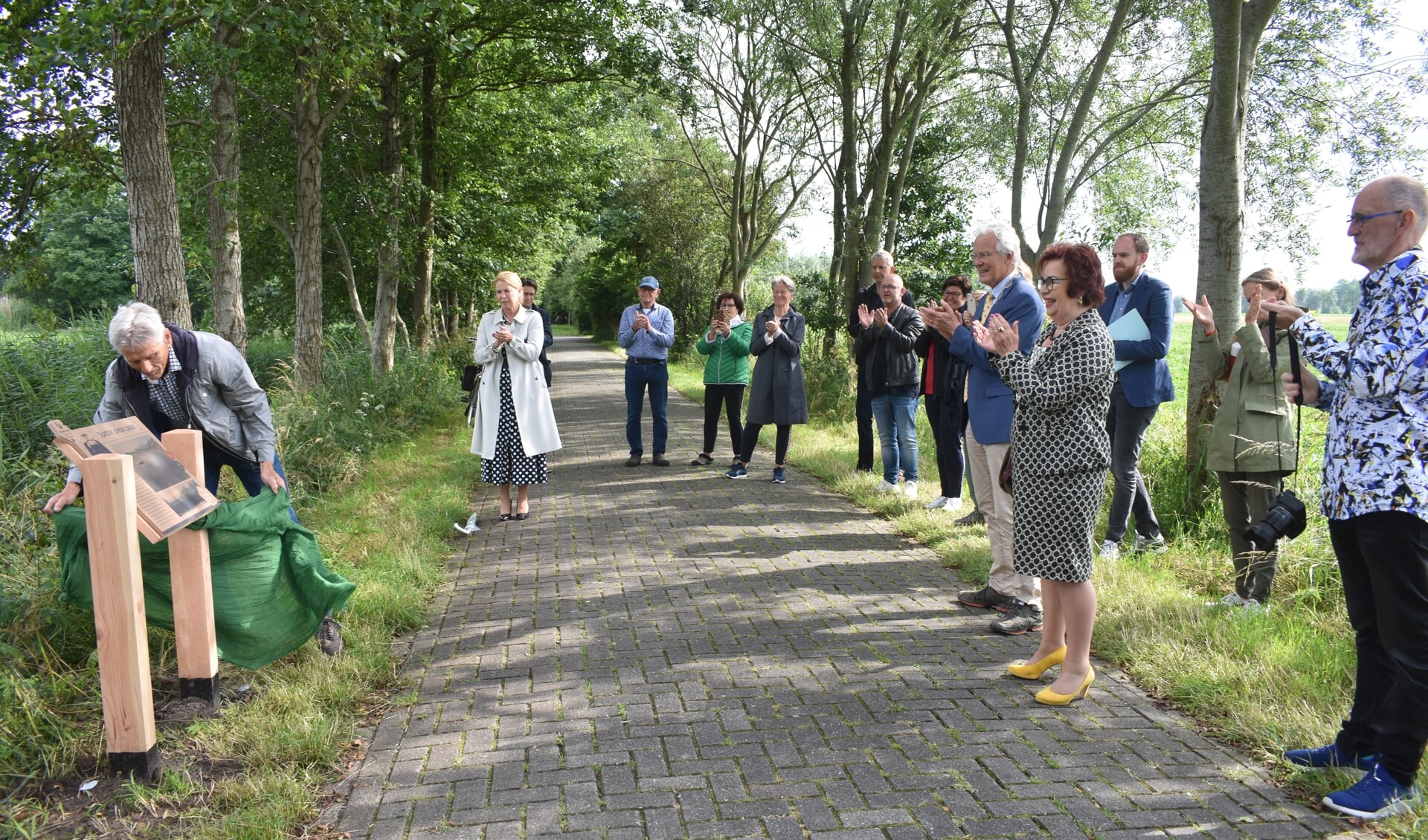 Voorzitter Lútsen Wijma van de lokale werkgroep opent de 'beleefroute'. Onder andere de bestuurders Avine Fokkens (witte jas), Jan Rijpstra (blauw jasje), Annet van der Hoek (WF) en Meindert de Boer (Doarspbelang) applaudiseren.