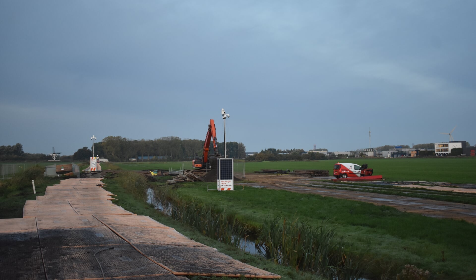 Links de transformator. Een machinist van Bijlsma BV ruimt de rijplaten in het weiland op. Rechtsachter bedrijventerrein De Hemrik in Leeuwarden.