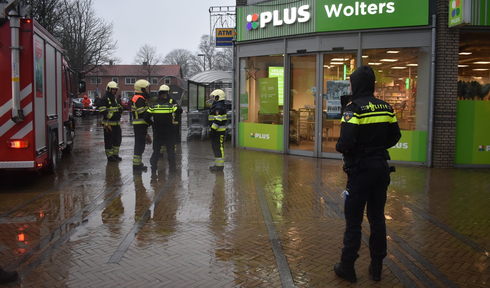 Brandweerlieden (mannen en vrouwen) in overleg met elkaar bij Plus Wolters in Burgum. terwijl een politievrouw toekijkt.
