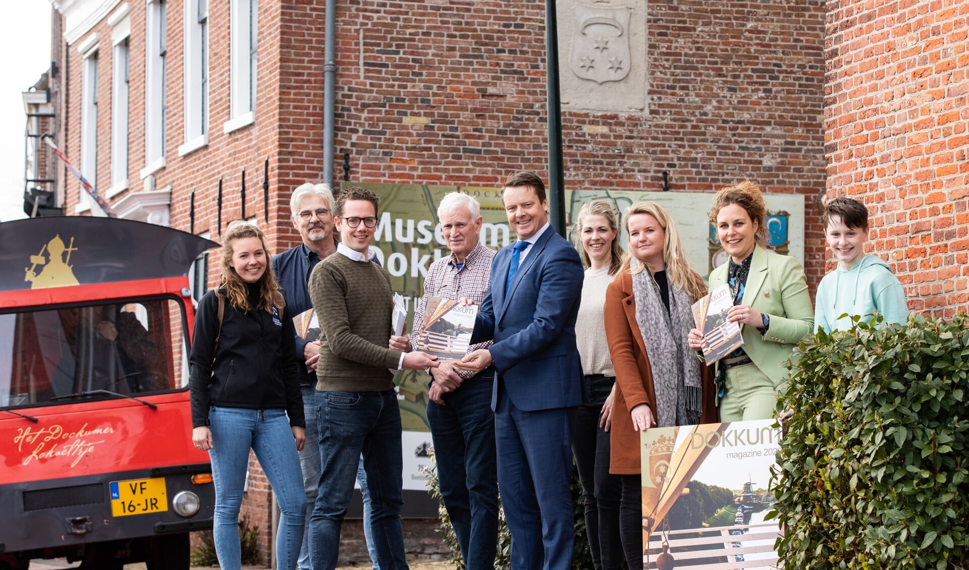 Burgemeester Johannes Kramer (in blauw pak) ontvangt het eerste exemplaar van Dokkum Magazine 2022 bij Museum Dokkum.