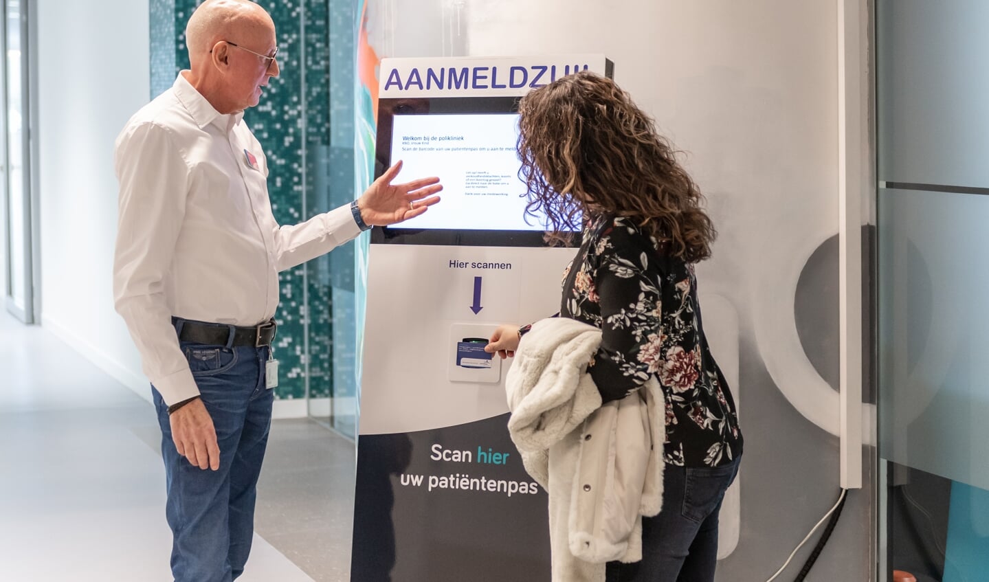 Vrijwilliger helpt een patiënt met het aanmelden voor een polikliniekbezoek via de aanmeldzuil.