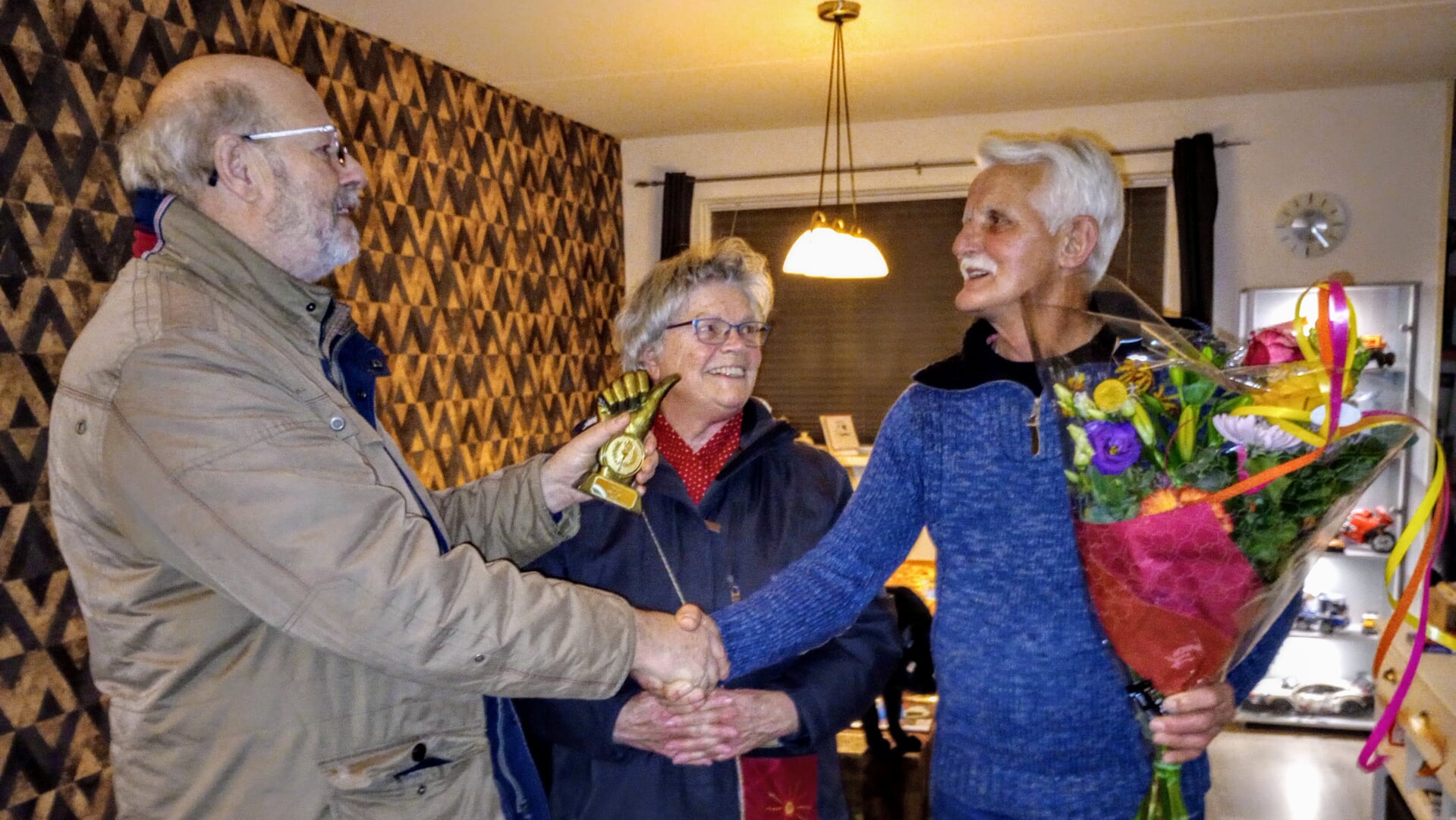 Geert van der Bij (rechts) ontvangt als Gariper fan it jier 2023 een bos bloemen en een 'gouden duim' uit handen van de redactie van dorpskrant De Rabbelskûte.