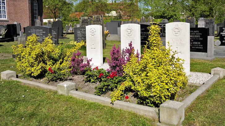 De drie oorlogsgraven op het kerkhof waar bloemen en een krans worden gelegd.
