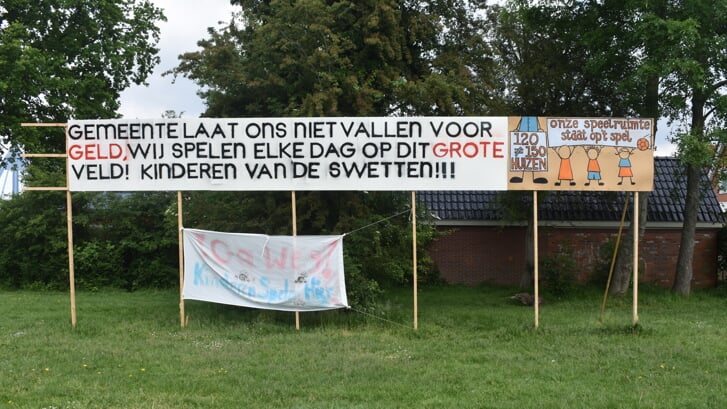 Protestborden en een protestvlag ('Ga weg! Kinderen spelen hier') op het terrein tegenover openbare basisschool De Swetten.
