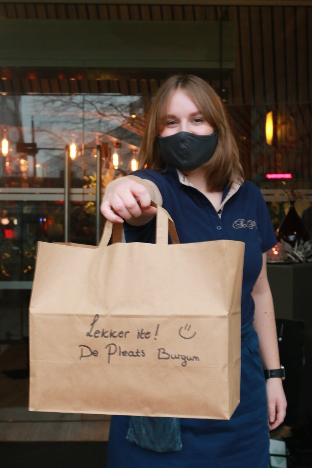 Een medewerker van Restaurant De Pleats overhandigt een afhaalmaaltijd. 