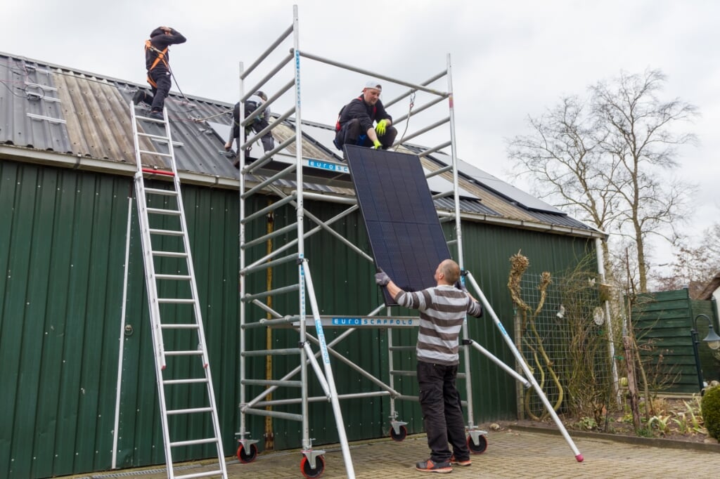 Wichard Dijkstra overhandigt een zonnepaneel aan zijn broer Peter-Martijn.Op het dak werken Zavino Bonifacia en Sebas Veenstra.