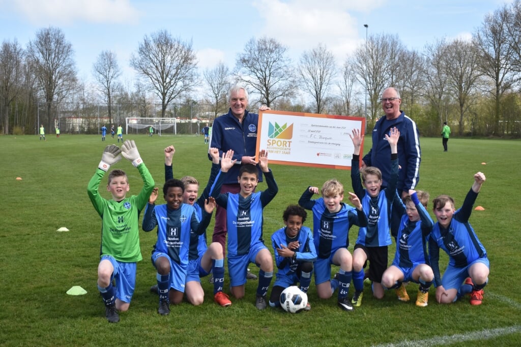 Het tweede team van jongens onder 12 jaar van FC Burgum is minstens zo blij met de prijs als twee vrijwilligers: gastheer Age Tolsma (linksachter) en jeugdtrainer Jan van Arkel.