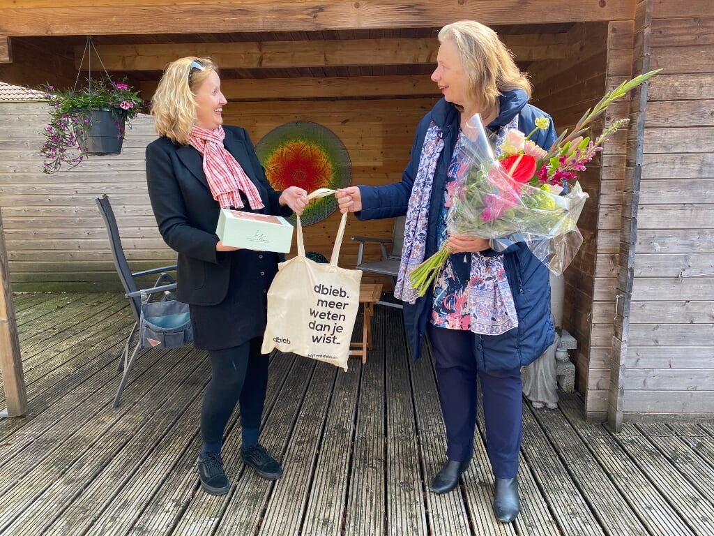 Foekje Meyer (rechts) krijgt niet alleen een tas met boeken (te leen), maar ook een bos bloemen en een taart, uit handen van Wilma Quarré, teamleider Tytsjerksteradiel van dbieb. 