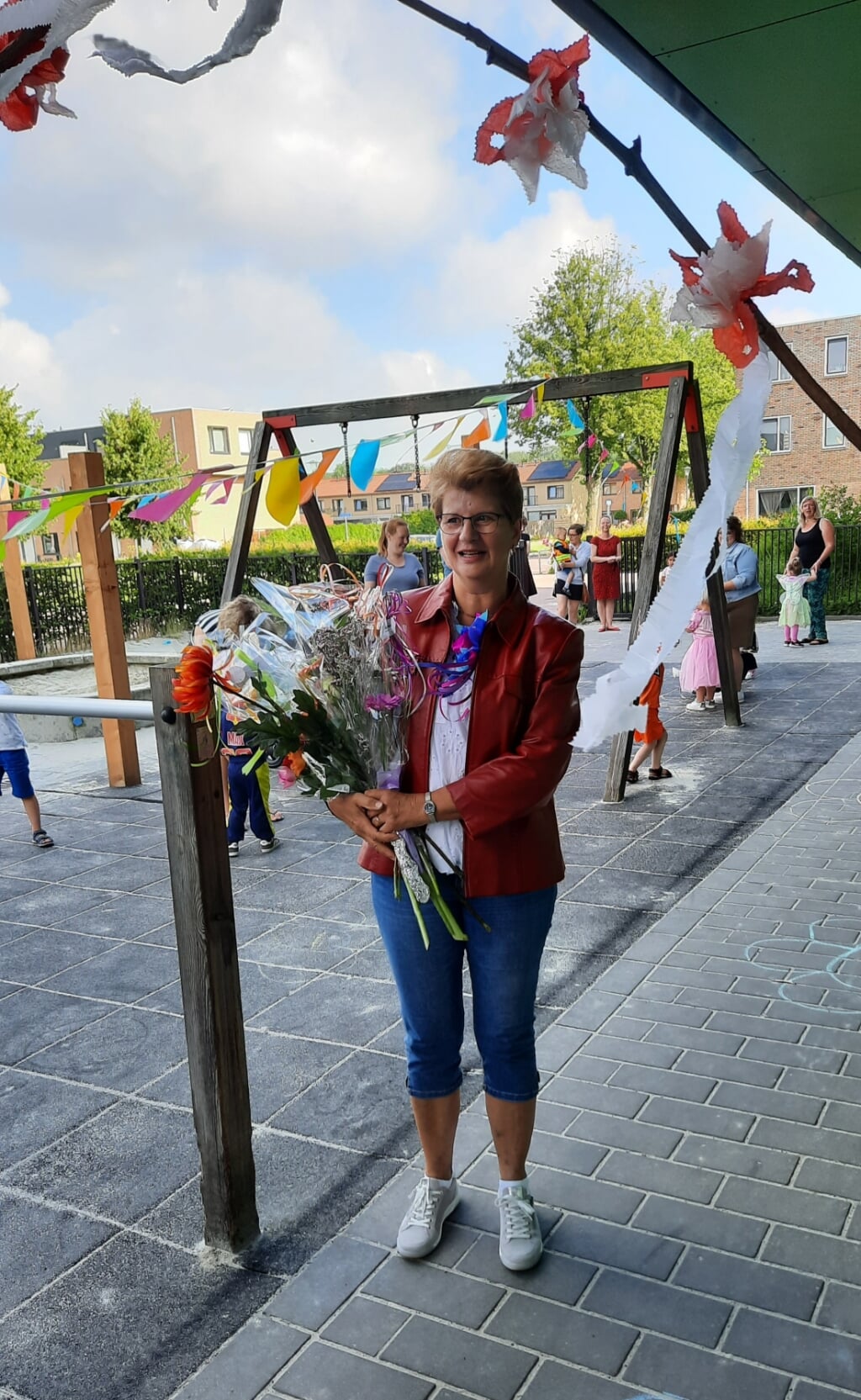 Juf Durkje van der Heide tussen kinderen, collega's en ouders, met een flink bos bloemen.