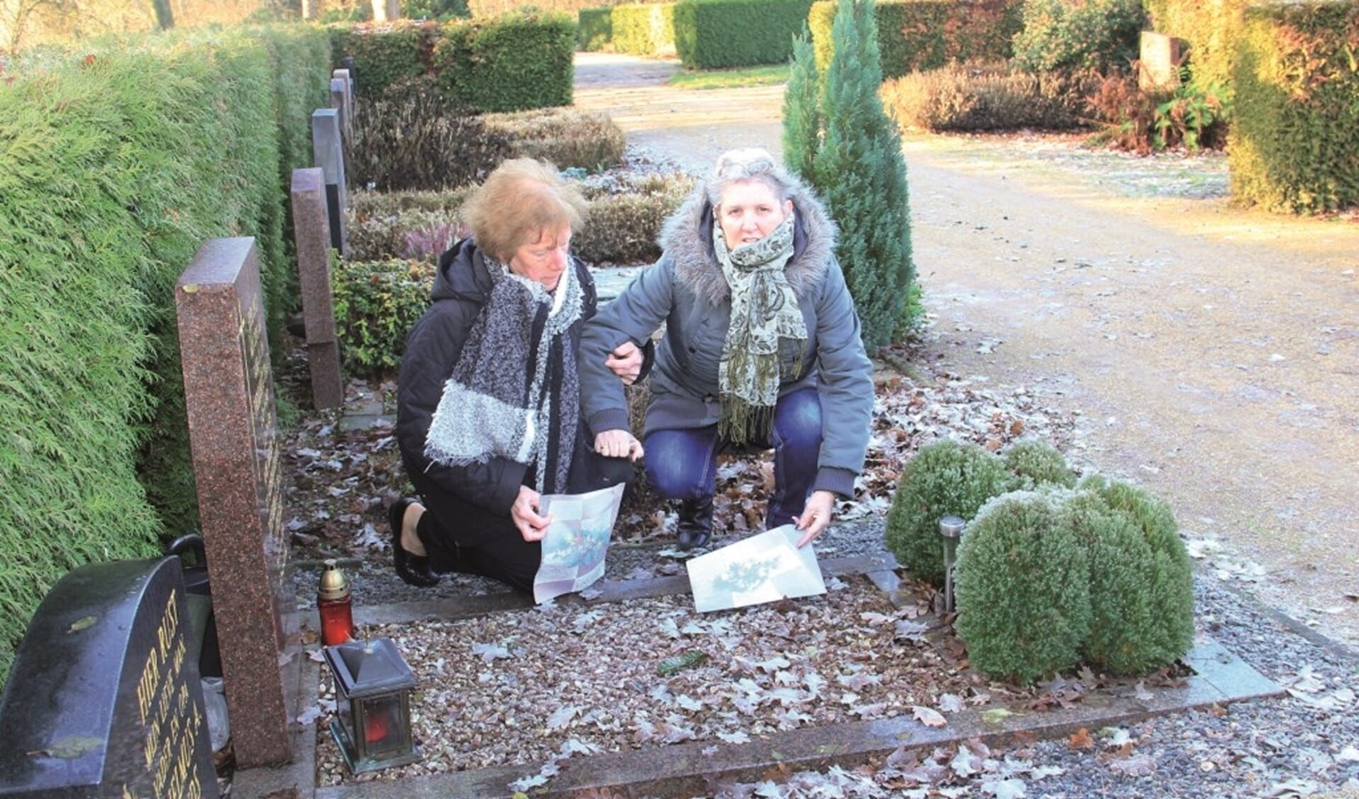 Marian Stienezen (rechts) en Dollie Willemsen bij een van de graven. In hun handen hebben ze foto's van de verdwenen kerststukken.