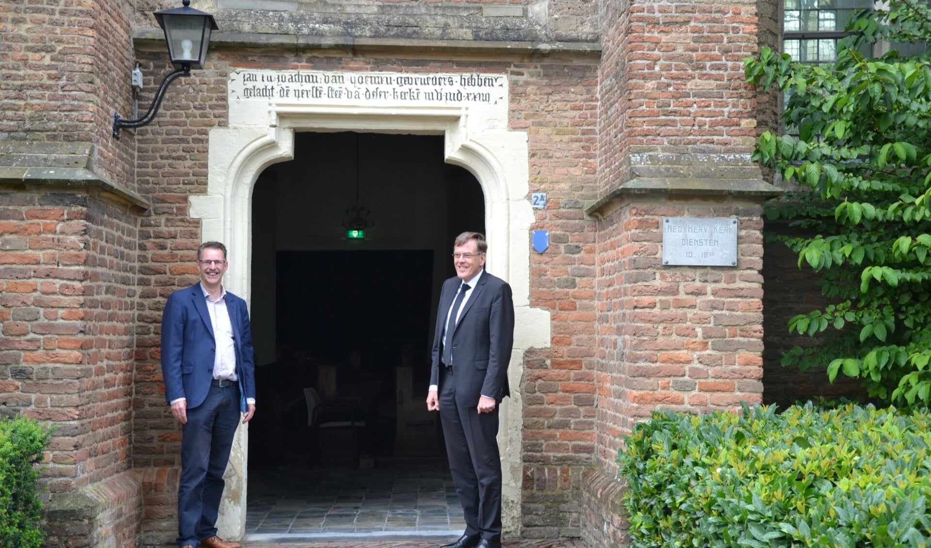 Bij de ingang van de kerk. Rechts staat de predikant van de gemeente, dominee R. van de Kamp en links Bart van Kleef, voorzitter van de evangelisatiecommissie. (foto: Nienke Heenck/HHK)