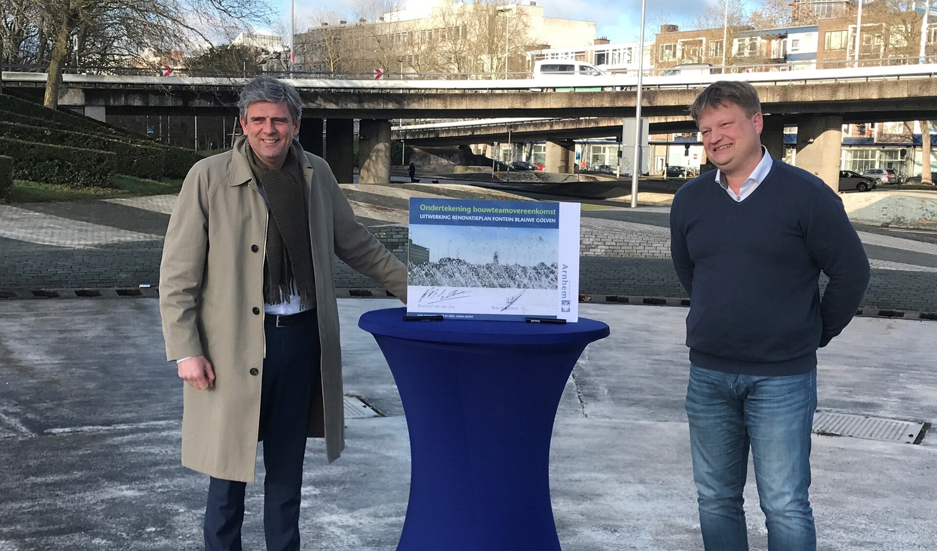 Wethouder Roeland van der Zee (links) en Hugo Rots, directeur Rots Maatwerk ondertekenen de overeenkomst in het midden van de fontein op de Blauwe Golven (foto: Gemeente Arnhem). 