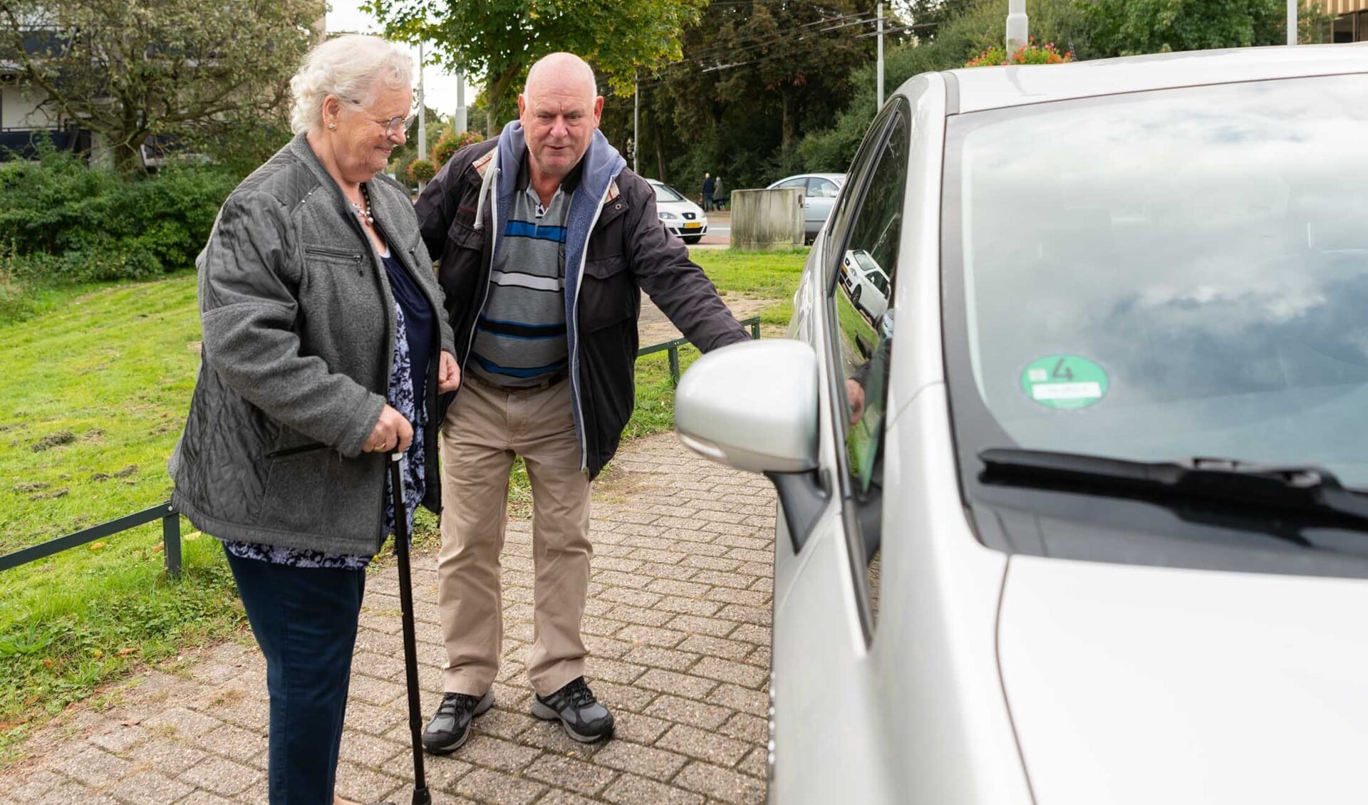 Een vrijwilliger van AutoMaatje helpt een oudere passagier bij het instappen.