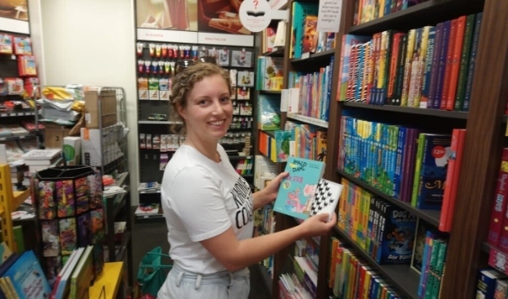 Rosalie van Woezik stopt in een boekenwinkel een aardige kaart in een kinderboek.