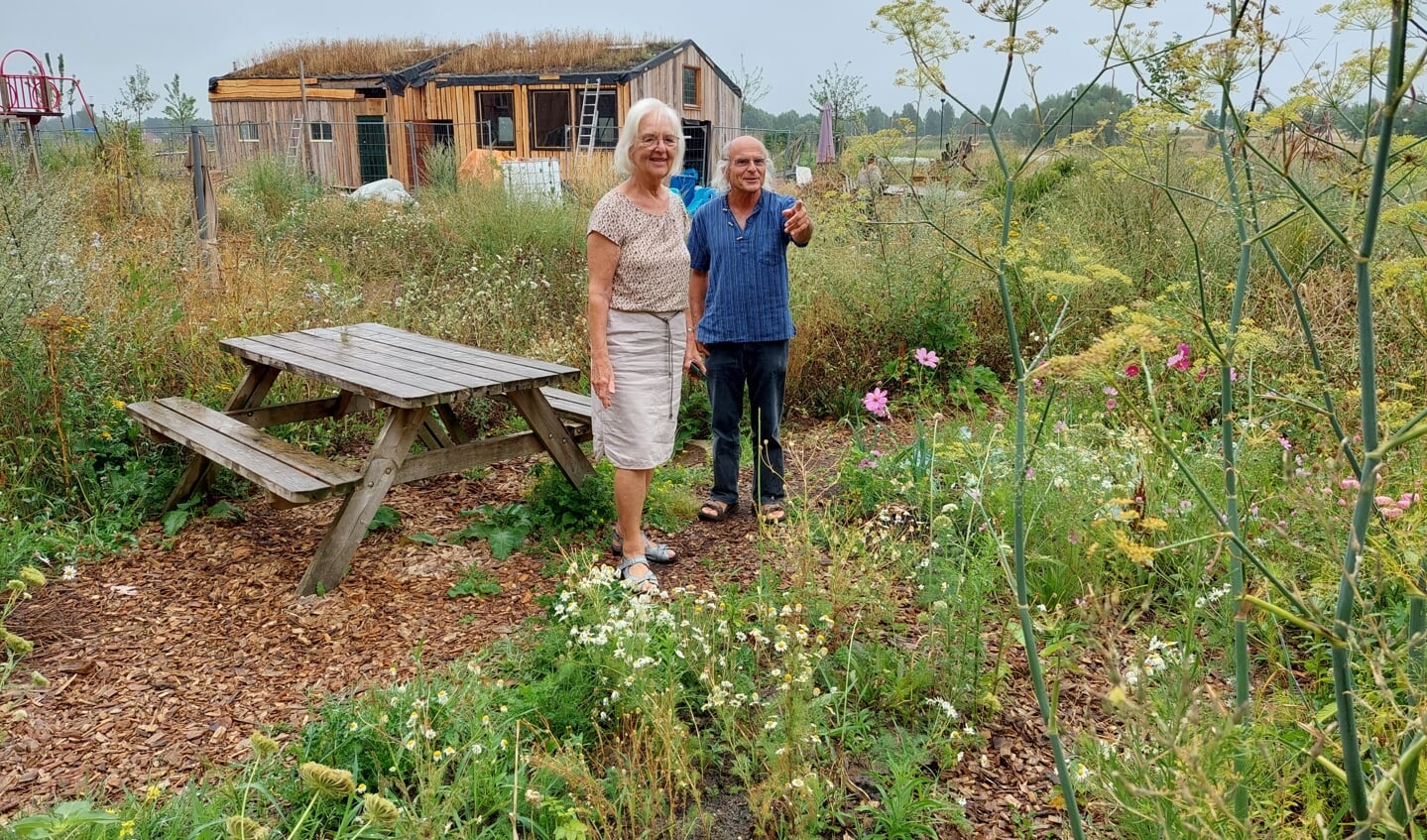 Hélène Bontjer en Ton Perry bewonderen de gemeenschappelijke tuin vol bloemen, kruiden en gewassen. Achter hen wordt gewerkt aan de schuur. 