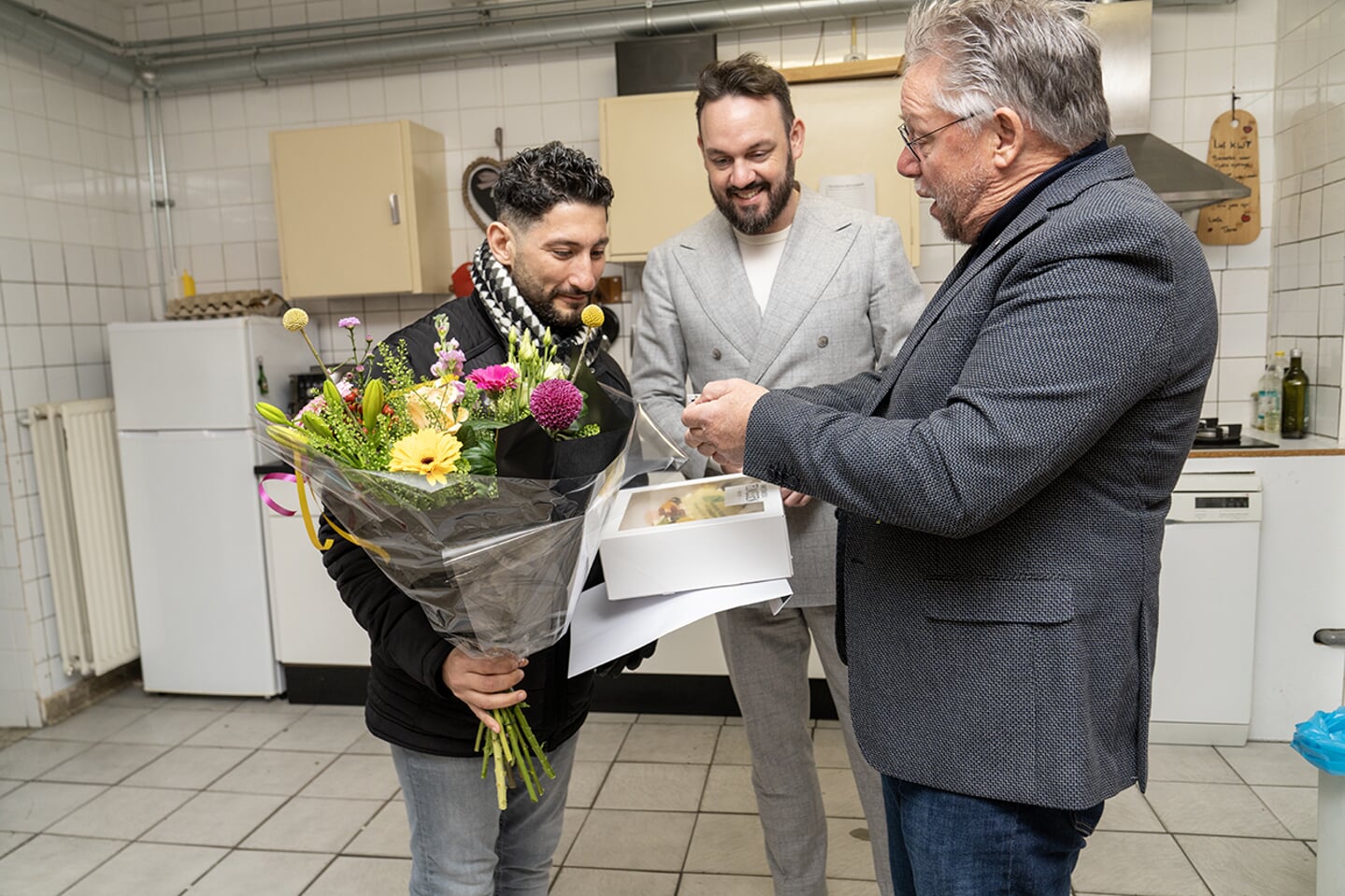 Genomineerde Toufic Al Arab ontvangt bloemen en taart uit handen van Chris van der Burg (Stichting Arnhemse Stadsprijs voor Vrijwilligerswerk) en Mark Lauriks (wethouder Vrijwilligersbeleid). 