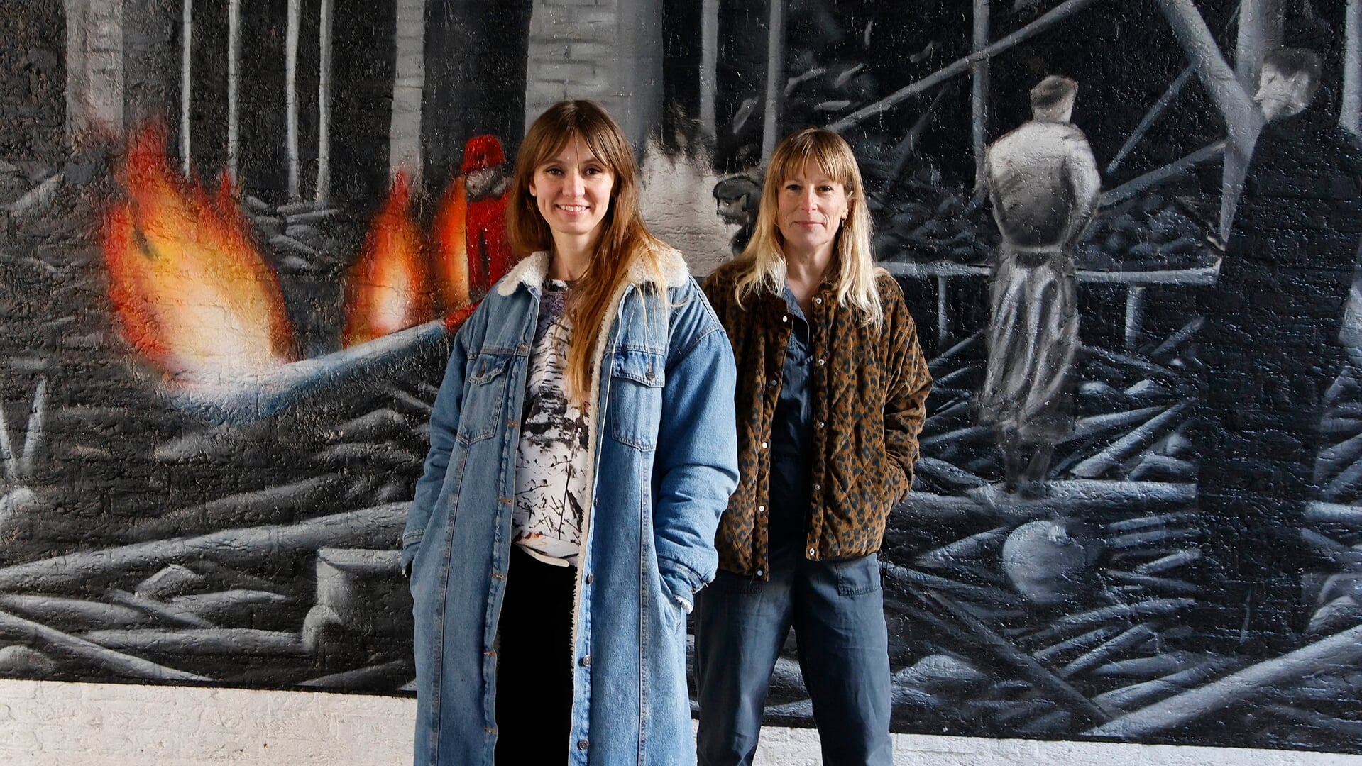 Annigje (links) en Sonja bij de muurschildering over het bombardement, te vinden in het steegje naast ICI Paris op Plein 1944. 
