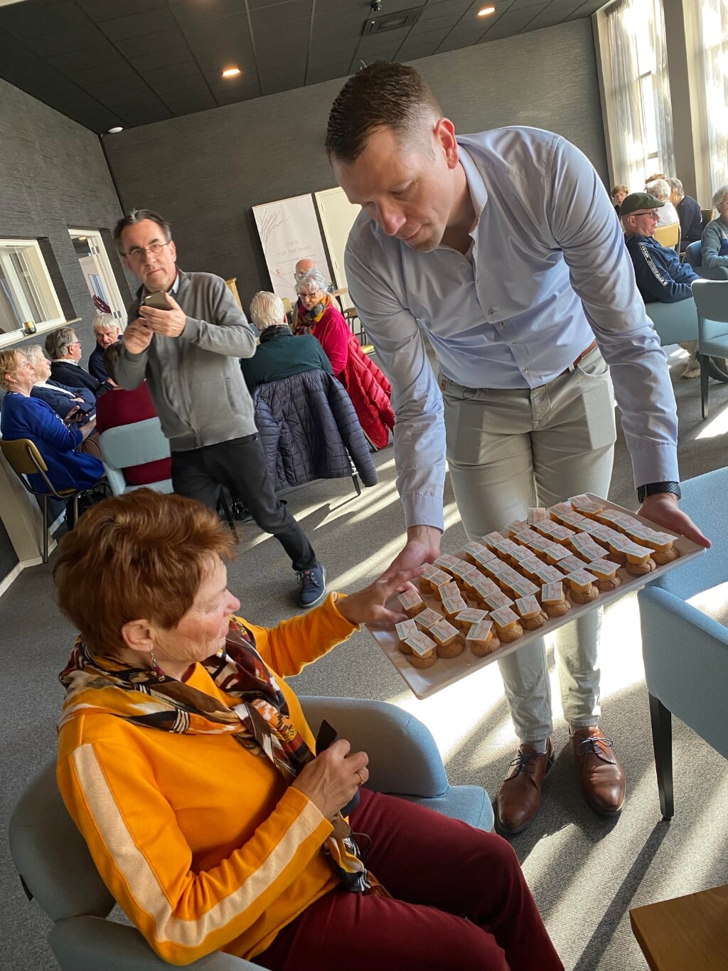 Wethouder Dimitri Horsthuis-Tangelder biedt Marijke van Brandenburger, bezoeker Huiskamer van Elst, een petit-fours aan voor bij de koffie. (foto: Hester van Aalst)