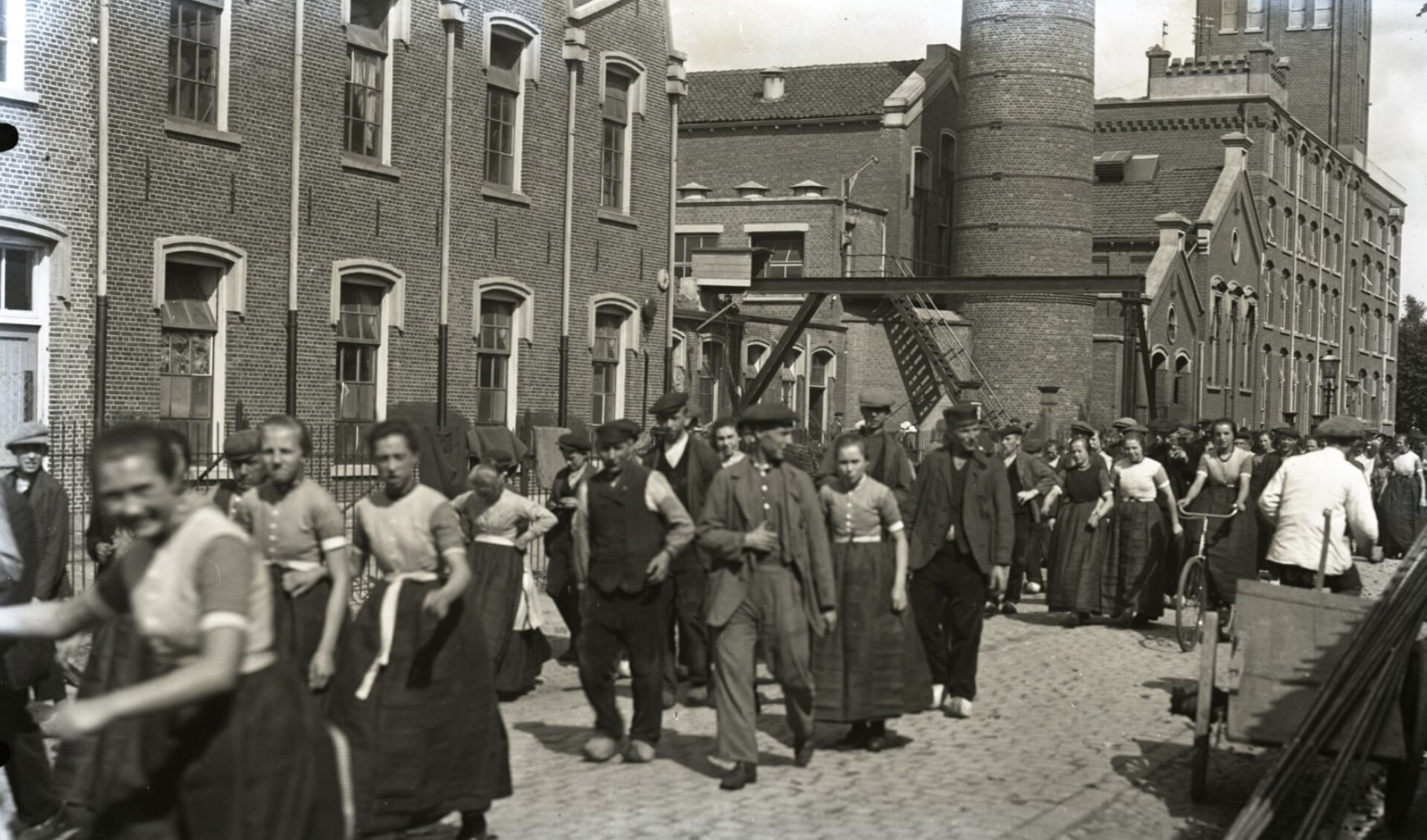 Een opname uit 1930 van het uitgaan van jutefabriek ’n Stoom aan de Wierdensestraat. De voorste vrouw is Gediene van Kosters (Boontn-Oarnd). Op de achtergrond fabriek De Beek (Bèkke) met het zogenaamde Engelse Werk. 