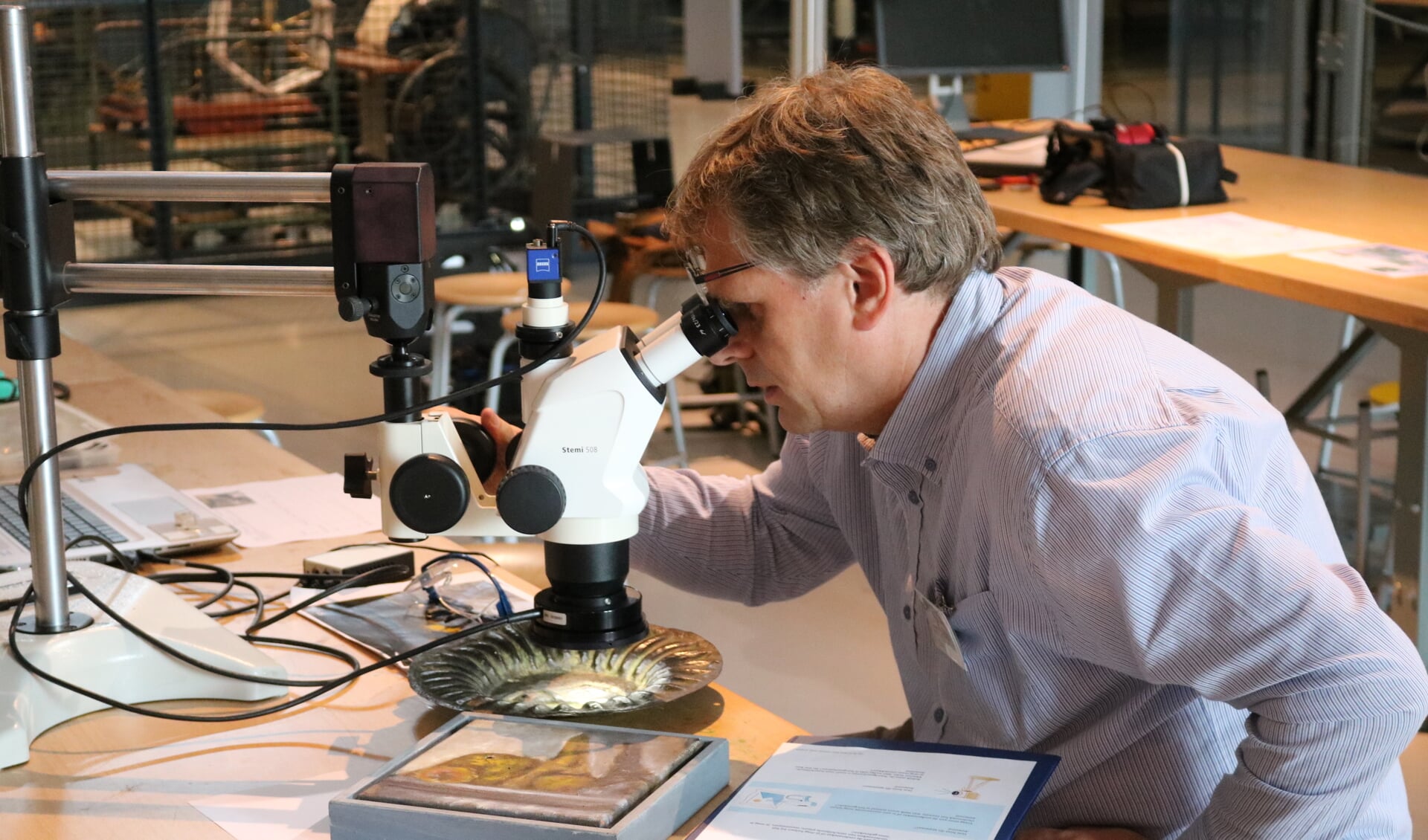 De onderzoeker van de Museumfabriek onderzoekt het bord onder een microscoop. 